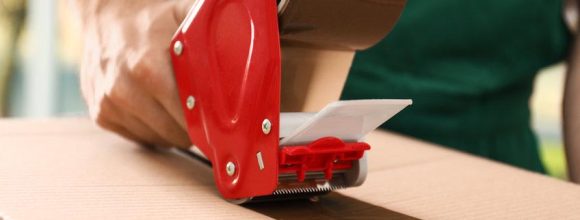 Man packing box with adhesive tape indoors, closeup. Moving serv