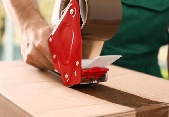 Man packing box with adhesive tape indoors, closeup. Moving serv